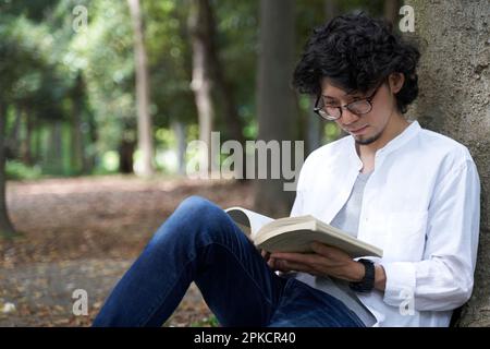 Man reading book sitting on tree back Stock Photo