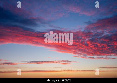 Fiery red and pink clouds paint the sky at sunset or sunrise. A beautiful, dramatic, and colorful skyscape, perfect as a natural background. Stock Photo