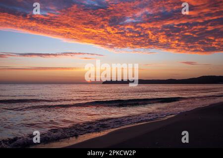 A spectacular, fiery sunrise paints the clouds orange and red over the Baltic Sea, viewed from a sandy beach on the island of Rügen, Germany. Stock Photo