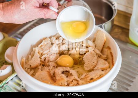 Good bourgeois housewife woman cook in kitchen pours eggs separated yolk from egg white with a cup to make bread dumplings with bread crumbs, Germany Stock Photo