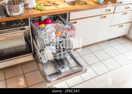 Close up of a fully stocked dishwasher in a kitchen with dishes glasses bowls knives forks spoons cutlery, Germany Stock Photo