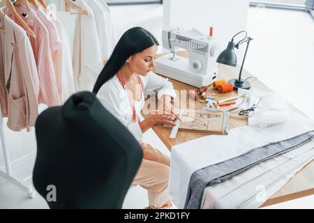 Sitting by the table. Seamstress is in her office that is with different clothes Stock Photo