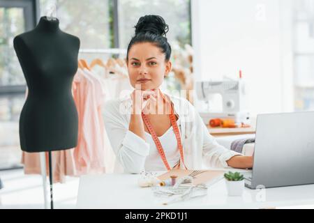 Working by using laptop. Seamstress is in her office that is with different clothes Stock Photo