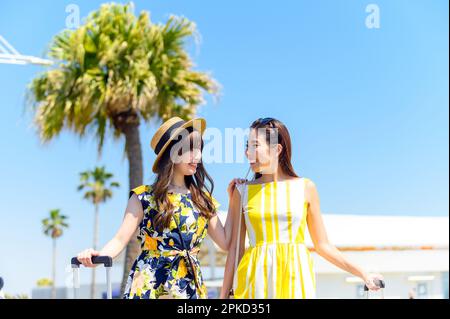 2 women traveling to a sea resort with a carry-on bag Stock Photo