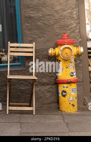 Yellow and Red Fire Hydrant covered in stickers outside a coffee shop next to an outdoor table and chair in Reykjavik, Iceland. Stock Photo