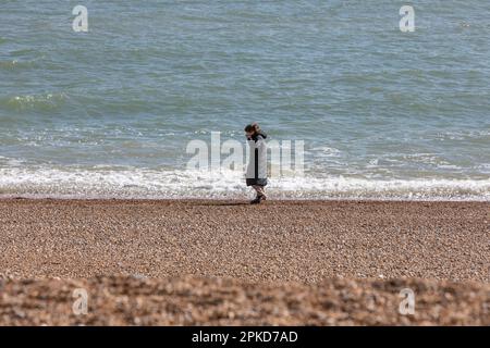 A young woman walking alone on a shingle beach near to the sea. Stock Photo