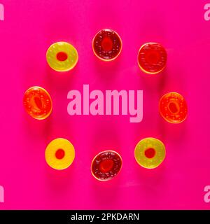 Circle of round jelly candies lie on vibrant pink background. Bright circular confections in variety of colors Stock Photo