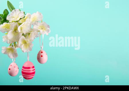 Three Easter eggs in shades of pink hanging from a branch in full bloom on a serene turquoise background Stock Photo