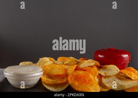 Side view of heap of potato chips with two dipping sauces on black slate serving board on grey plaster table. Sophisticated Chip and Dip Duo Stock Photo