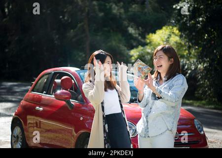 Two women taking a picture in front of a car Stock Photo