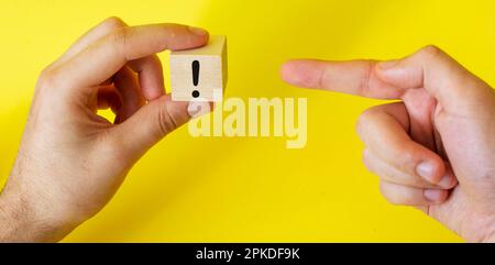 an exclamation mark drawn on a block of wood that a man holds in his hand and the index finger points to the sign Stock Photo