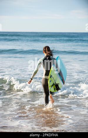 Woman in wetsuit running with surfboard Stock Photo