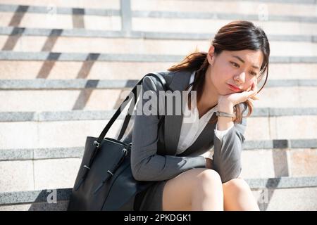 Woman in suit sitting on stairs thinking Stock Photo