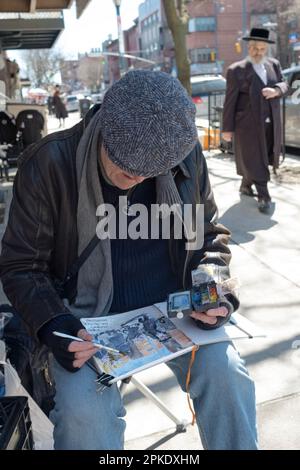 A Jewish man in a cap paints pictures of Jewish life on Lee avenue in Williamsburg, just before Passover 2023. In Brooklyn, New York. Stock Photo