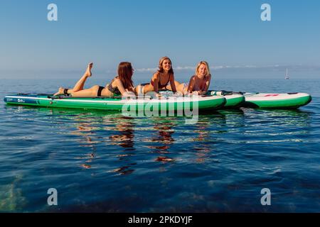 July 30, 2022. Budva, Montenegro. Attractive young girls on stand up paddle board at sea with morning sun light. Women relaxing on Red Paddle SUP boar Stock Photo