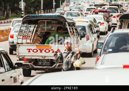 Yangon, Myanmar - March 25, 2023 : Myanmar man walking down on the street to sell food and drink in Yangon traffic jam. real local people lifestyle. Stock Photo