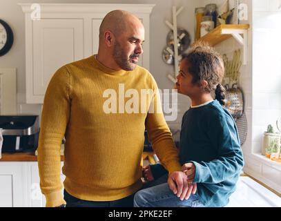 Loving father talking to son with Down syndrome sitting on counter Stock Photo