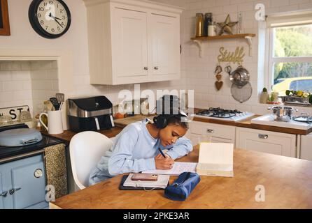 Teen girl doing homework and using phone texting in kitchen Stock Photo