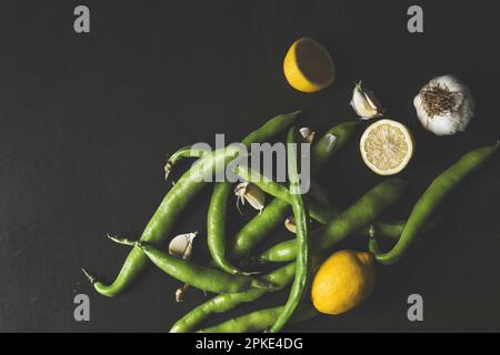 Fresh green faba beans with lemon and garlic on black rustic background, table top shot Stock Photo
