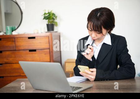 Woman in suit looking at her phone at home Stock Photo