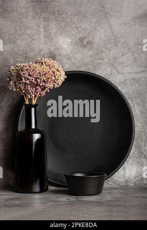 Black round dish, black bowl and a bottle with garlic flowers on a gray stone background Stock Photo