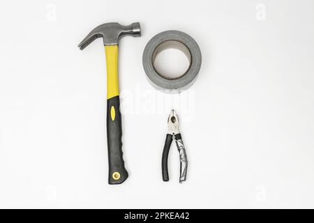 A pair of pliers, a roll of gray adhesive tape and a carpenter's hammer on a white surface Stock Photo