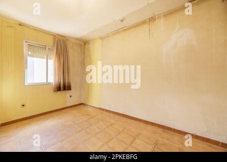 A room in an apartment in poor condition in need of a good coat of paint on the walls and a window with old curtains Stock Photo