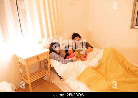 Three parents and a child reading to each other in bed Stock Photo