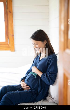 Pregnant woman sitting on bed touching her stomach Stock Photo