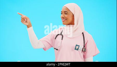 Face, nurse and Muslim woman pointing to mockup in studio isolated on a blue background. Portrait, healthcare professional and happy Islamic person Stock Photo