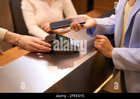 Female worker helping fashionable visitor with contactless payment at desk Stock Photo