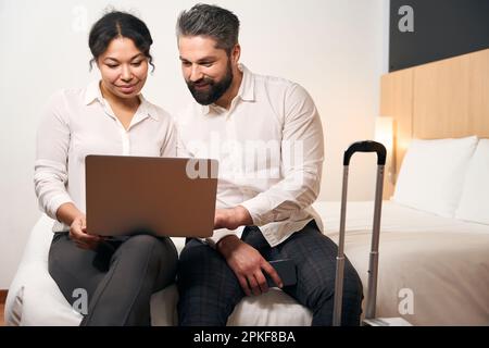 Young couple seated in hotel room looking at computer monitor Stock Photo