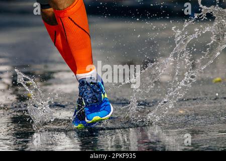 close-up legs male runner in compression socks running puddle on road, splashes and drops from under your feet Stock Photo
