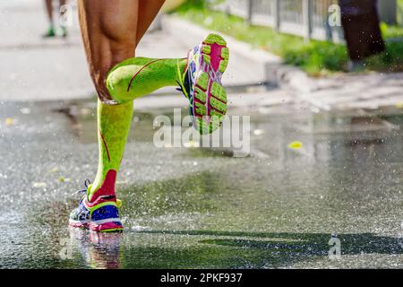 legs male runner in green compression socks running water on road, splashes and drops from under your feet Stock Photo