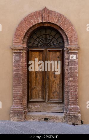 Well worn arched doorway with wooden double doors in Tuscany Stock Photo