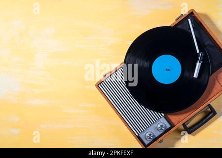 Old gramophone with a vinyl record on yellow wooden table, top view, vintage style. Stock Photo
