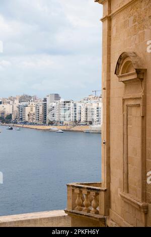 Valletta, Malta - November 12, 2022: Limestone corner house with a bricked up window and a baluster balcony with a view on Sliema town Stock Photo
