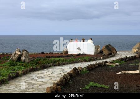 Four people sitting on a stone bench looking out over the Atlantic Ocean near the Faro De Pechiguera lighthouse, Lanzarote. Taken February / Stock Photo