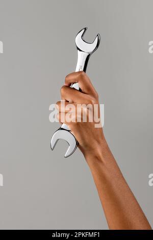 Anonymous African American female demonstrating metal spanner in raised arm against gray background Stock Photo