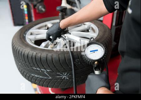 Crop male worker of garage service pumping up balanced automobile tire using pressure gauge in car workshop Stock Photo