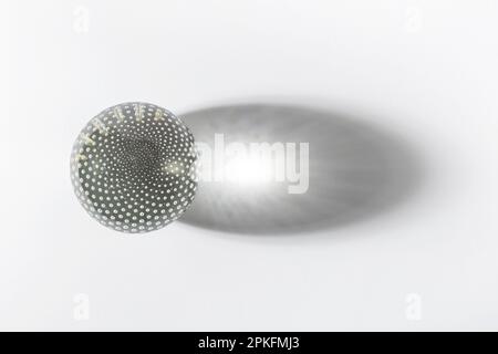 Decorated disco ball with spots on surface made of glass casting large shadow against white backdrop Stock Photo