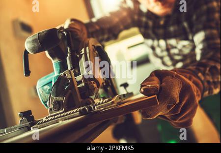 Caucasian Construction Worker Cut Wooden Plank to Size Using Circular Cordless Saw. Close Up Photo. Construction Industry Theme. Stock Photo
