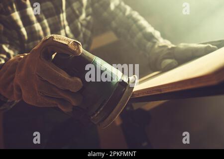 Worker Softening Plank Edges Using Wood Sander Close Up. Construction Theme. Stock Photo