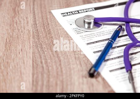 Close-up of a stethoscope and pen over a health report over a wooden table. Stock Photo