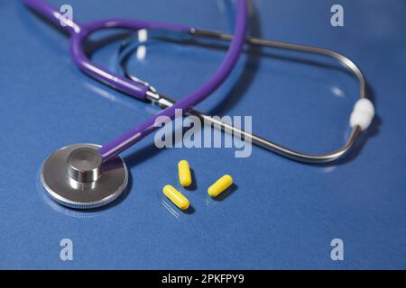 Close-up of a stethoscope's bell three yellow pills over a blue reflective surface. Stock Photo