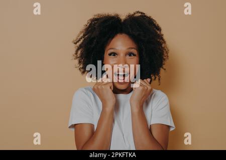 Portrait of excited amazed young woman keeping mouth opened and screaming with enjoyement, clenching fists, celebrating victory and success while posi Stock Photo