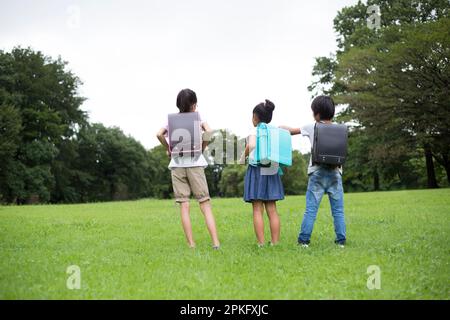 Elementary school children standing in a meadow with their school bags on their backs Stock Photo