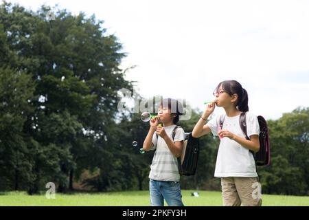 Elementary school students with school backpacks playing with soap bubbles in a meadow Stock Photo