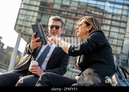 Two business people meeting outside and using a tablet, sunny light effect Stock Photo