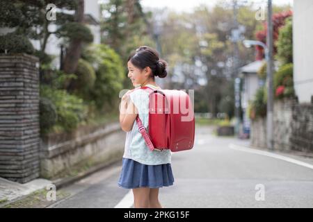 Girl with School Bag Walking in Residential Area Stock Photo
